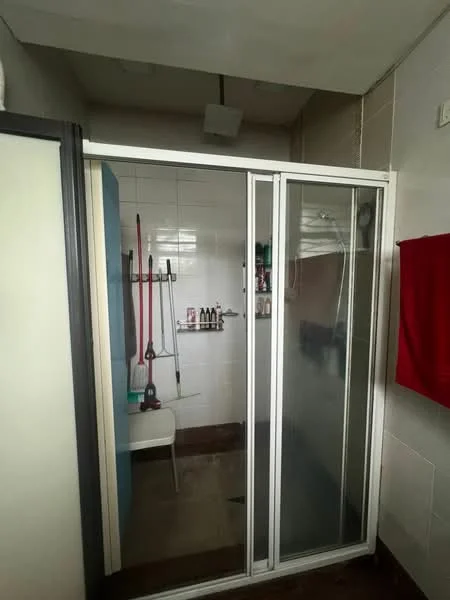 Bathroom features: glass shower enclosure, white tiled walls, grey tiled flooring, shower head, shower caddy with toiletries, red towel hanging, white stool, wall-mounted storage shelf.