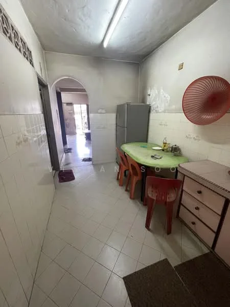 Kitchen features: green table with chairs, white tiled walls, white tiled flooring, stainless-steel fridge, wooden cabinet, red wall fan, sink, doorway leading to another room.