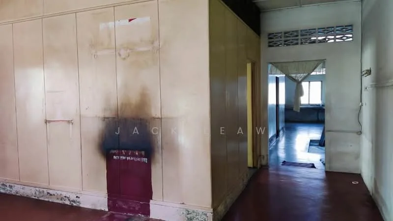 Room features: painted walls with stains, red flooring, window with sheer curtains, wooden door, exposed ceiling, partition wall, visible corridor, flooring transitions.