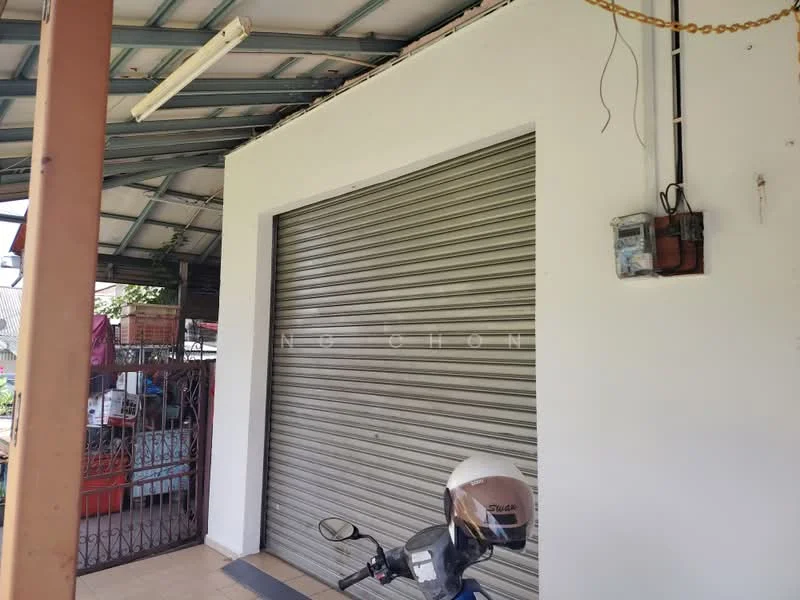 Exterior features: metal roller shutter door, white painted wall, roof with metal sheeting, exposed electrical wiring, concrete flooring, motorcycle parked.