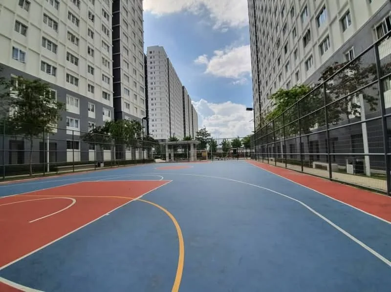 Exterior type: high-rise condominium; features: basketball court, multi-storey residential buildings, manicured landscaping, fenced perimeter, outdoor lighting, play area, surrounding greenery, blue and red court markings; style: modern.