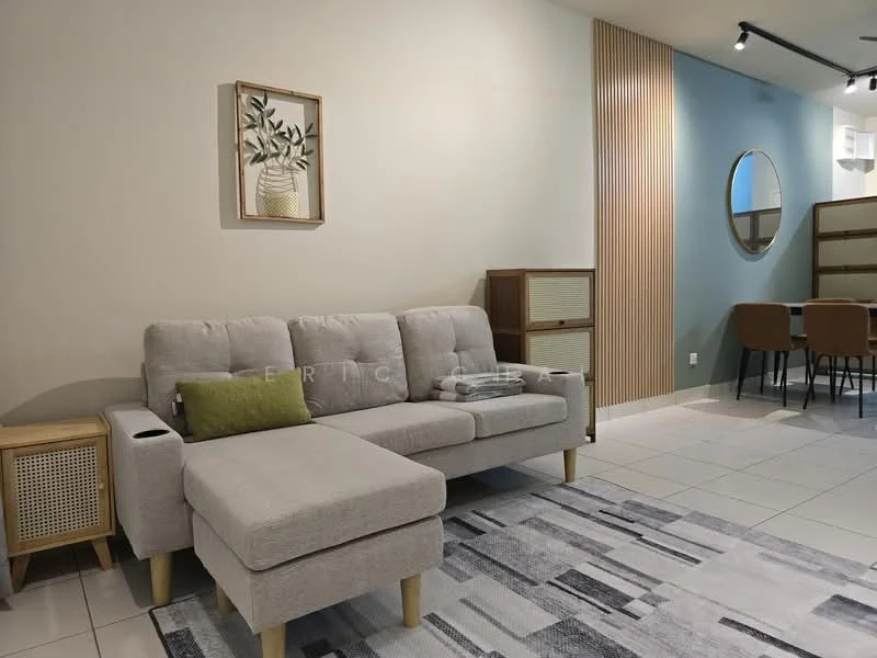 Living features: light grey fabric sofa with chaise, green accent cushion, area rug with geometric pattern, wooden side table, wall-mounted artwork with plant design, wood panel accent wall, round mirror, dining table with chairs visible in background, white painted walls, recessed lighting, tile flooring; style: modern.