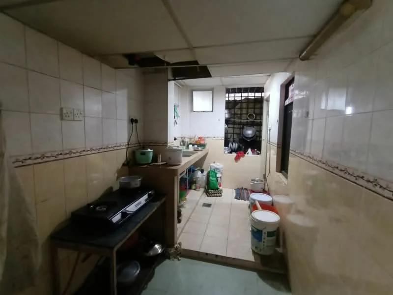 Kitchen features: white tiled walls, cream tiled flooring, stainless-steel gas stove, wooden countertop, sink with faucet, open shelving, multiple plastic buckets, kitchen utensils, window for natural light, exposed ceiling, wall-mounted storage, floor-mounted cabinets.