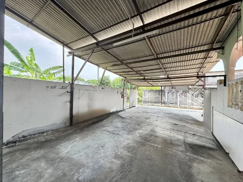 Exterior type: car porch; features: covered car porch, concrete flooring, metal roof, open space, surrounded by walls, banana trees visible in background; style: modern.