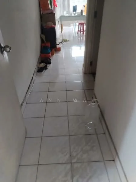 Hallway features: glossy white tile flooring, plain white walls, door leading to another room, visible electrical outlets, light source from adjacent room, cluttered with boxes and items, narrow corridor layout.