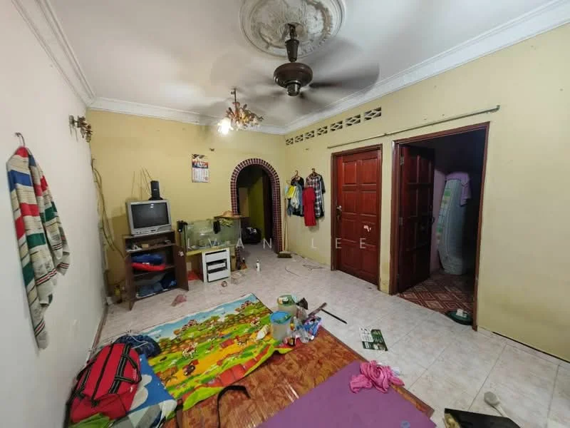 Living features: cream painted walls, white ceiling with decorative rose, 5-blade ceiling fan, tile flooring, TV unit, television, green plastic storage unit, colorful play mat, clothes hanging on wall, doorway leading to other rooms, rug on floor, backpack on floor, various items scattered on floor.