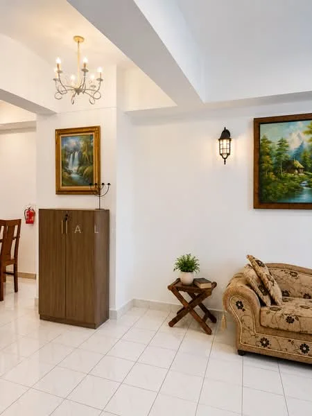 Living features: white painted walls, white ceiling, chandelier with multiple bulbs, wall-mounted sconce, ceramic tile flooring, sofa with floral pattern, wooden side table, framed artwork on wall, decorative plant in ceramic pot, wooden cabinet, dining table in background; style: contemporary.