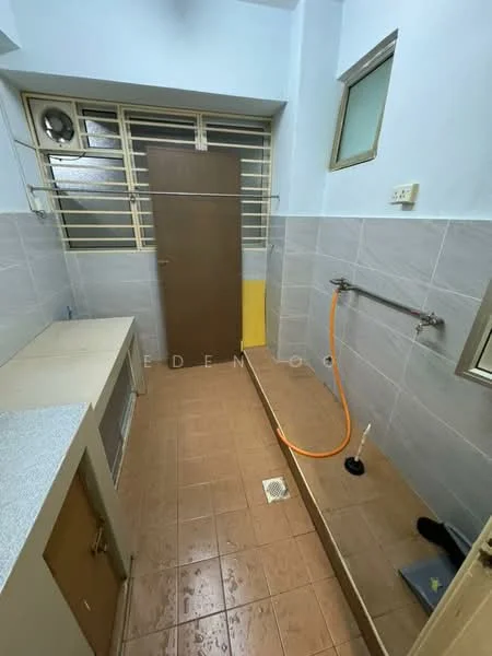 Laundry features: grey tiled walls, brown tiled flooring, single-basin laundry sink, wall-mounted faucet, drainage floor grate, window with metal grille, wooden door, countertop with grey surface, orange hose, yellow wall section.
