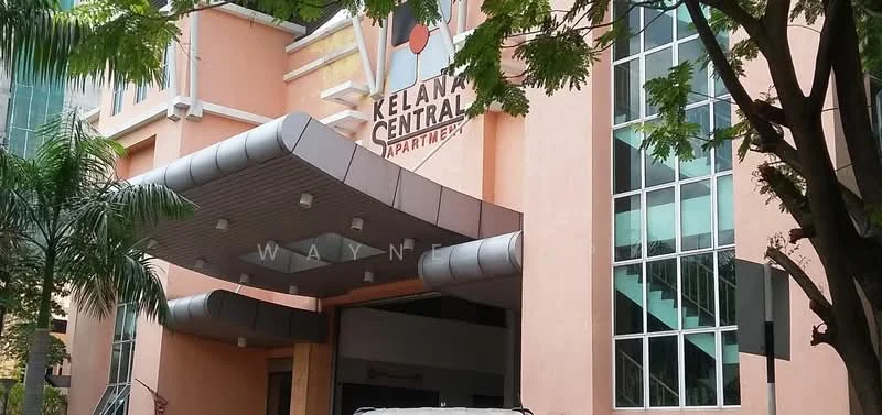 Exterior type: low-rise apartment block; features: pink painted facade, glass windows, covered entrance with awning, staircase visible, palm trees in landscaping, signage with 'Kelana Central Apartments', modern architectural design; style: modern.
