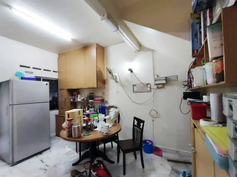 Kitchen features: stainless-steel fridge, wooden cabinetry, white walls, marble flooring, table with four black chairs, kitchen countertop, wall-mounted electrical outlets, overhead fluorescent lighting, cluttered countertop with various kitchen items.