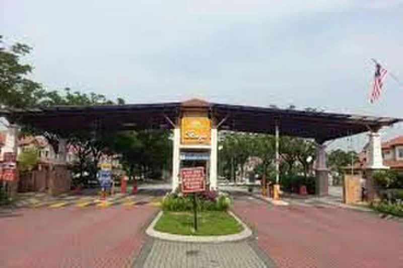 Exterior type: main entrance gate; features: covered entrance with solar panels, paved driveway, landscaped garden with flowers, security booth, traffic signage, flagpole with Malaysian flag, gated entry, surrounding trees; style: modern.