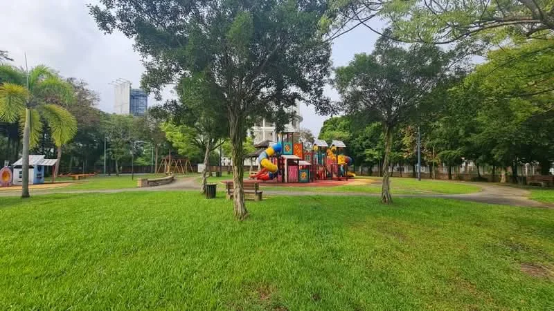 Exterior type: landscape garden; features: manicured lawn, mature trees, children's playground with colorful equipment, paved walking paths, benches, surrounding greenery; style: modern.