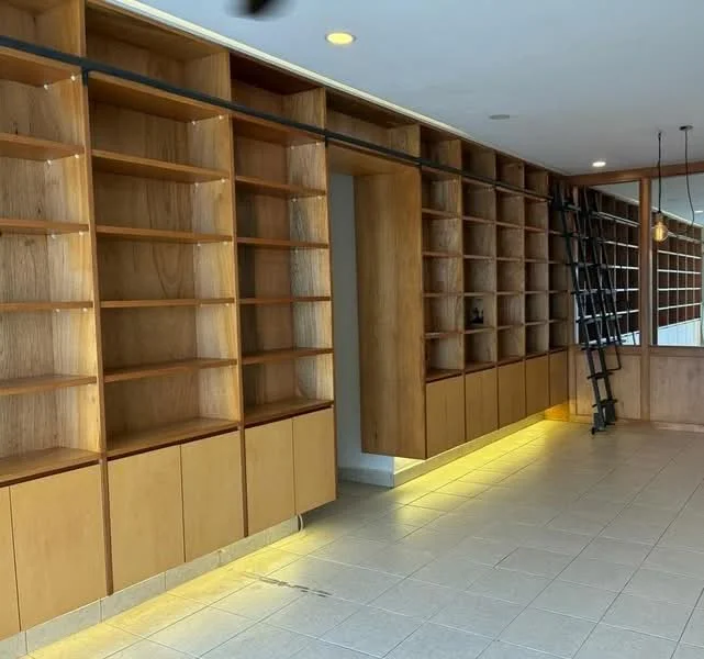 Room features: built-in wooden shelving, light wood cabinetry, open shelving units, floor tiles in light color, LED strip lighting under shelves, metal ladder for access, smooth wall surface, recessed ceiling lights; style: modern.