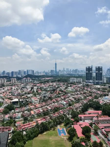 Exterior type: high-rise condominium; features: city skyline view, surrounded by residential areas, green spaces visible, sports court visible, high-rise buildings in background, low-rise houses in foreground; style: modern.
