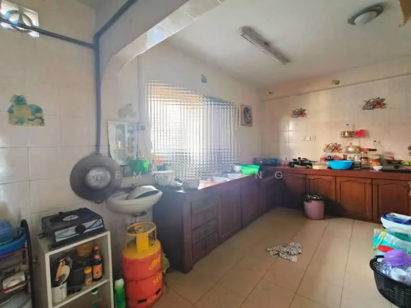 Kitchen features: brown wooden cabinetry, white tiled walls, light beige tiled flooring, stainless-steel sink, chrome faucet, gas stove with hood, countertop with food preparation area, window with metal grille, various kitchen utensils and containers, green plastic trash bin, yellow gas cylinder.