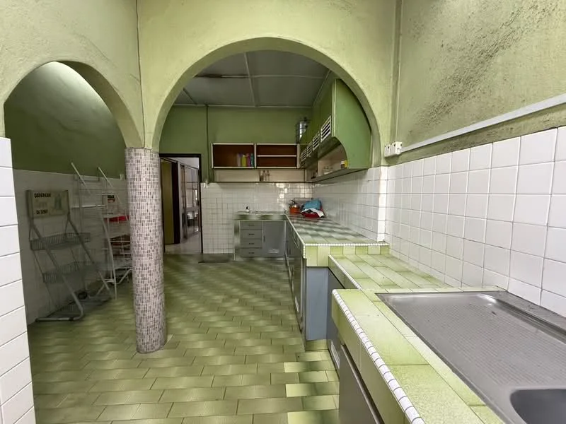 Kitchen features: green tiled flooring, white tiled walls, arched entryway, stainless-steel sink, chrome faucet, grey cabinetry, built-in oven, countertop with green tiles, open shelving, kitchen island, exposed ceiling, utility area with drying rack.