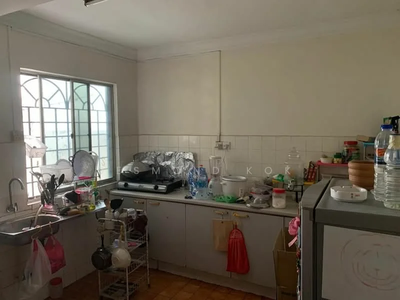 Kitchen features: single-bowl stainless-steel sink, chrome pull-down faucet, white tiled backsplash, grey cabinetry, countertop with clutter, kitchen appliances visible, multiple plastic containers, floor tiles in orange, window with decorative grille, dish rack with dishes, water bottles on countertop, various utensils and kitchenware.