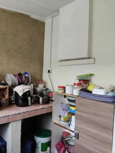 Kitchen features: pink countertop, wooden cabinetry, stainless-steel range hood, various kitchen utensils, stacked plates, plastic containers, kettle, cooking pots, green bucket, multiple storage jars.