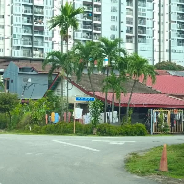 Exterior type: high-rise condominium; features: multiple-storey building, balconies visible on upper floors, surrounded by greenery, palm trees in foreground, residential area, road intersection in front, fenced garden area, clothes hanging on lines; style: modern.