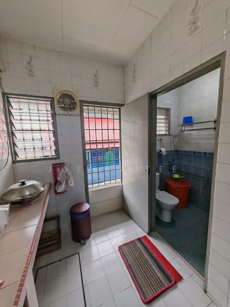 Bathroom features: white tiled walls, white tiled flooring, toilet, sink, shower area, window with metal grille, mirror, shelf, blue bucket, red trash bin. Laundry features: countertop, stainless-steel sink, cabinet, floor mat.