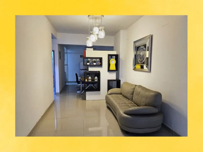 Living features: grey leather curved sofa, glass coffee table, pendant lighting with multiple bulbs, white painted walls, glossy ceramic tile flooring, decorative wall art, black shelving unit, yellow wall clock; style: modern. Dining features: dining table for four, black dining chairs, white walls, ceramic tile flooring; style: modern.