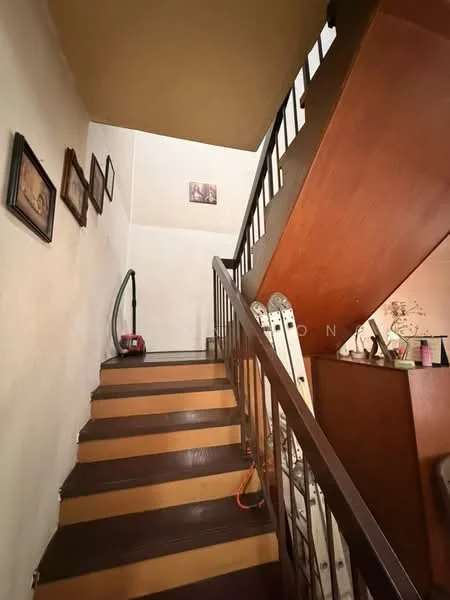 Room features: wooden staircase with dark brown treads, white painted walls, ceiling with light brown color, framed artwork on walls, vacuum cleaner visible, ladder visible, handrail on staircase, natural light from upper level; style: traditional.