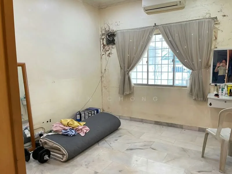 Room features: white painted walls with visible damage, marble flooring, floor-to-ceiling window with sheer curtains, wall-mounted split AC, mirror on dressing table, dressing table with chair, rolled-up mattress on the floor, clothes on the floor, decorative wall with peeling paint.