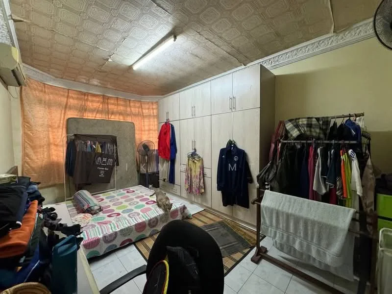 Bedroom features: white painted walls, textured ceiling with pattern, tile flooring, built-in wardrobe with sliding doors, foldable mattress on the floor, clothes hanging on a rack, two standing fans, curtains covering the window, area rug, office chair.