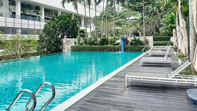 Exterior type: swimming pool deck; features: infinity pool, pool deck with loungers, tropical landscaping, manicured hedges, palm trees, water feature, wooden decking, surrounding greenery; style: modern.
