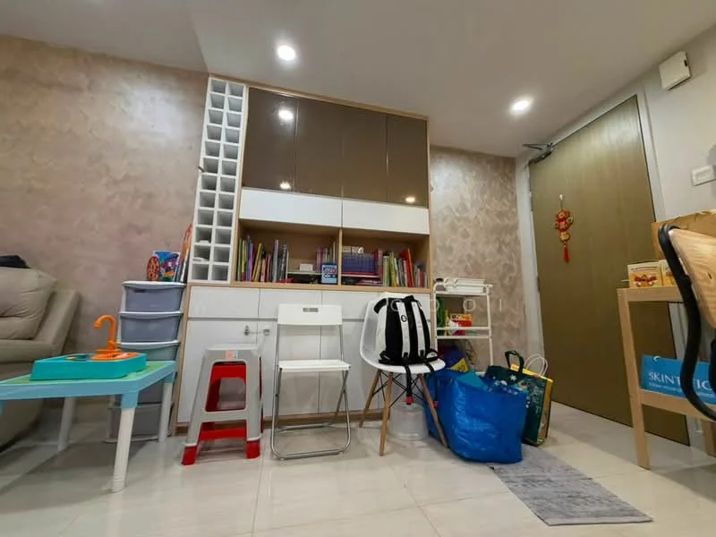 Room features: cream wallpaper with geometric pattern, white built-in shelving unit, wooden desk with drawers, white folding chair, beige leather sofa, blue children's table, red children's chair, various bags and toys, white storage cabinet, light-colored tiled flooring, recessed LED downlights, main entrance door; style: modern.
