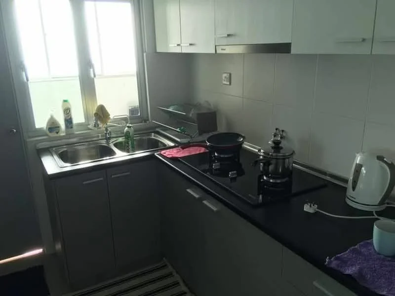 Kitchen features: double-bowl stainless-steel sink, chrome pull-down faucet, black countertop, grey cabinetry, built-in gas stove, stainless-steel kettle, glass splashback, window with sheer curtains, cleaning supplies on countertop, kitchen towel on countertop, striped floor mat; style: modern.