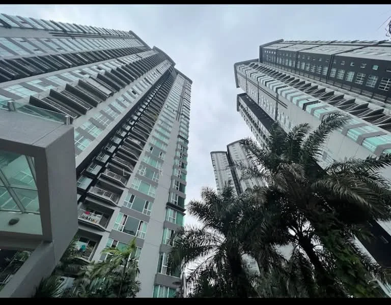 Exterior type: high-rise condominium; features: glass curtain wall, balconies with glass railings, tropical landscaping with palm trees, multiple storeys, modern architectural design, surrounded by greenery, cloudy sky, urban context; style: modern.