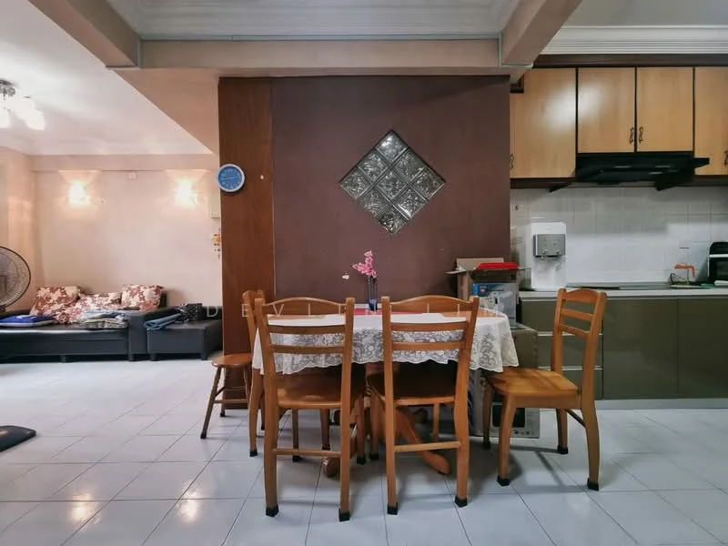 Dining features: wooden dining table with lace tablecloth, 4 wooden dining chairs, decorative flower vase on table, wall-mounted clock, cream tiled flooring, brown accent wall, glass block window, open kitchen area visible, kitchen cabinetry in light wood, white countertop, kitchen appliances visible; style: modern. Living features: fabric sofa with floral pattern, throw pillows, blankets on sofa, wall-mounted light fixtures, cream painted walls; style: modern.