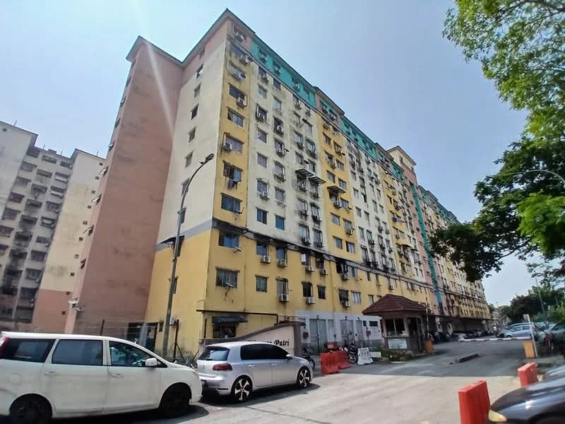 Exterior type: low-rise apartment block; features: yellow painted facade, multiple balconies, visible air conditioning units, ground-level parking area, entrance with awning, surrounding greenery, adjacent road access, multi-storey structure; style: modern.