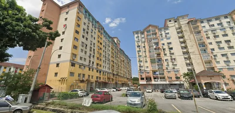 Exterior type: low-rise apartment block; features: multi-storey building, yellow and cream painted facade, balconies on upper floors, parking lot with multiple vehicles, surrounding greenery, street view, visible utility lines, adjacent buildings, entrance with signage; style: modern.