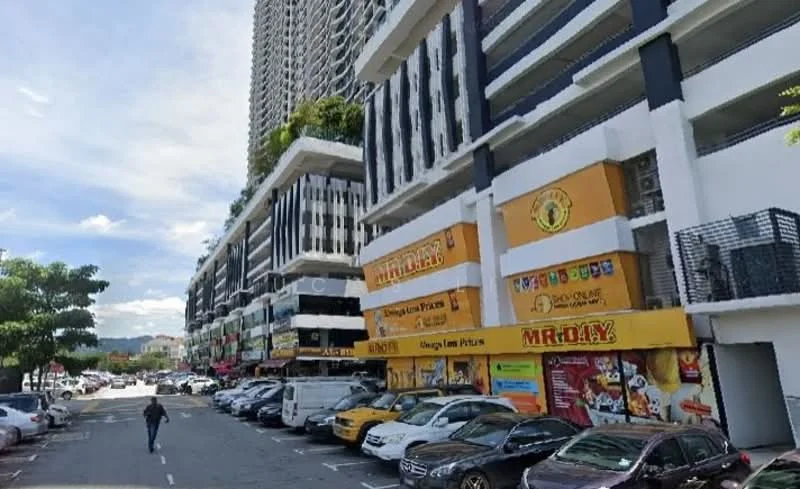 Exterior type: mixed-use development; features: multi-storey building, ground floor retail units, outdoor parking area, various signage for businesses, trees along the sidewalk, modern architectural design, balconies on upper floors, street view with cars parked, clear blue sky, urban setting; style: modern.
