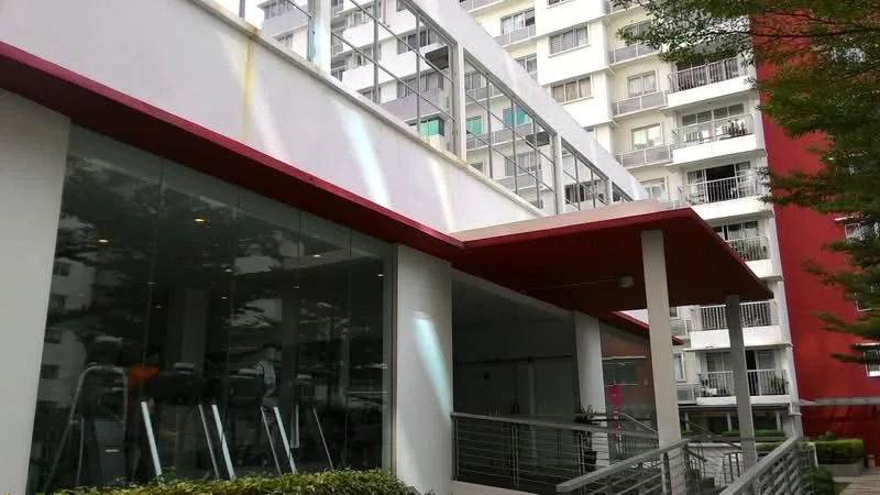Exterior type: mid-rise condominium; features: glass facade, red accent roof, outdoor gym area, manicured landscaping, balconies visible on upper floors, metal railing, large windows, greenery around the building; style: modern.