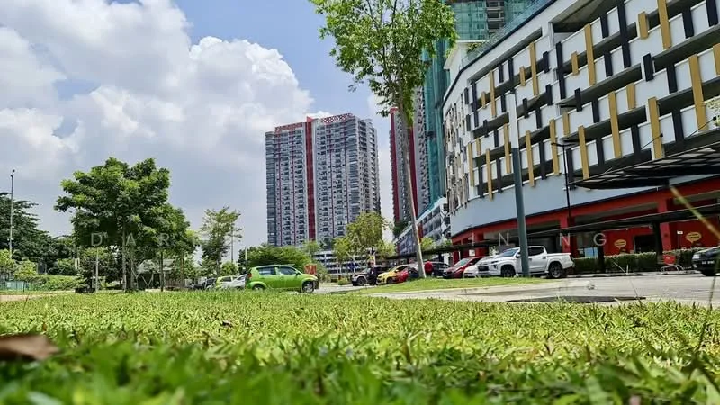 Exterior type: high-rise condominium; features: glass curtain wall, red accent facade, surrounded by landscaped greenery, manicured lawn, multiple storeys, parking lot with visible cars, trees in vicinity, urban setting; style: modern.