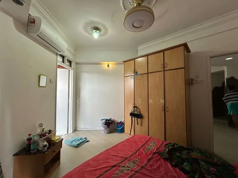 Bedroom features: wooden flooring, white painted walls, ceiling fan with light, 1 wall-mounted split AC, built-in wardrobe with wooden finish, bed with red bedding, small bedside table, window with sheer curtains, laundry basket, bottle of water, towel on the floor.