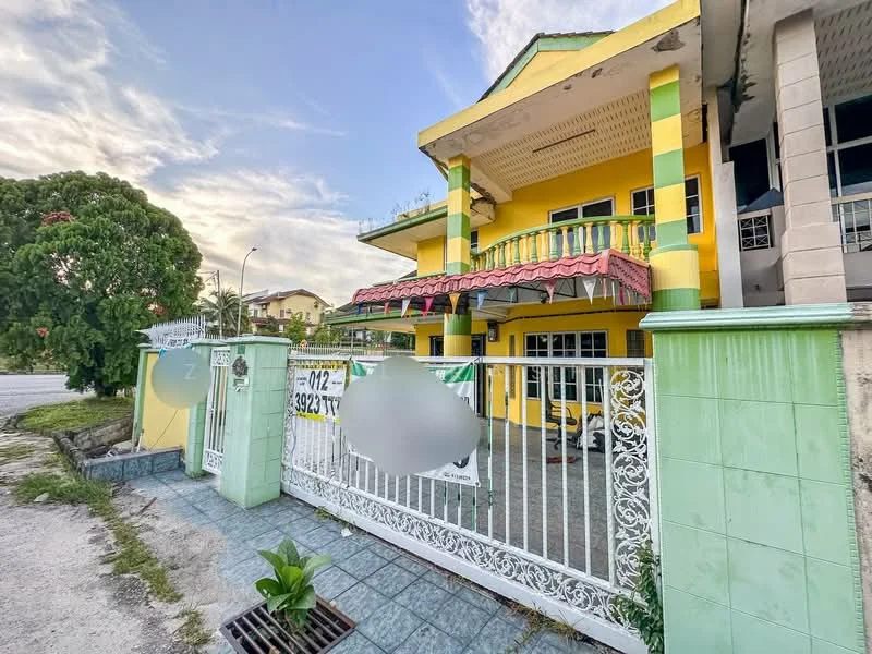 Exterior type: semi-detached house; features: yellow painted facade, green accent columns, gated entrance with wrought iron fence, covered porch with awning, paved driveway, manicured lawn, surrounded by greenery, two-storey structure, balcony on upper floor; style: modern.