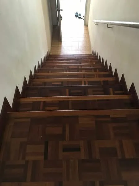 Room features: wooden staircase with patterned steps, handrail, tiled flooring at the base, light-colored walls, natural light from doorway.