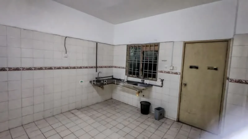 Kitchen features: white tiled walls, grey tiled flooring, single-bowl stainless-steel sink, chrome faucet, window with metal grille, wooden door, countertop with backsplash, waste bin, plastic trash can.
