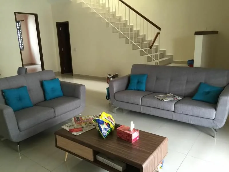 Living features: 2-seater fabric sofa in grey, 3-seater fabric sofa in grey, blue accent cushions, wooden coffee table, magazines on coffee table, tissue box on coffee table, white walls, tile flooring, staircase in background, natural light from windows, open layout; style: modern.