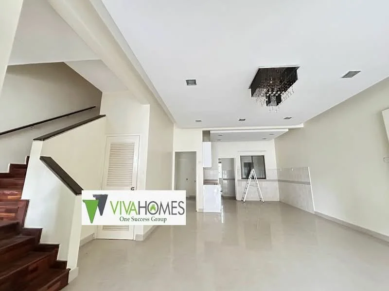 Living features: white painted walls, polished tile flooring, chandelier, staircase with wooden steps, recessed ceiling lights, open layout to kitchen, kitchen area visible in background, large windows for natural light; style: modern.