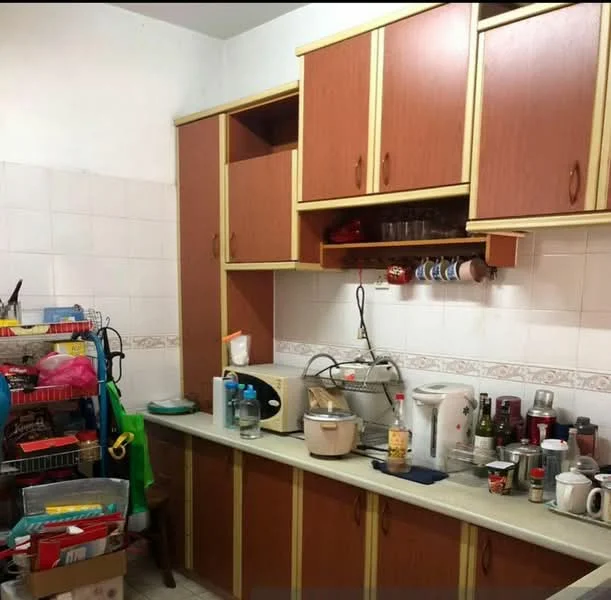 Kitchen features: wood cabinetry with yellow trim, light green countertop, white tiled backsplash, stainless-steel sink, chrome faucet, built-in wall shelves, various kitchen appliances, multiple containers and utensils, open shelving with dishes, flooring with light tiles.