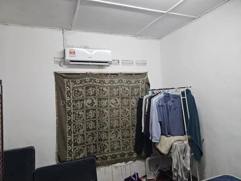 Room features: white painted walls, ceiling with grid tiles, 1 wall-mounted split AC, clothes rack with hanging clothes, decorative fabric hanging on wall, flooring not visible.