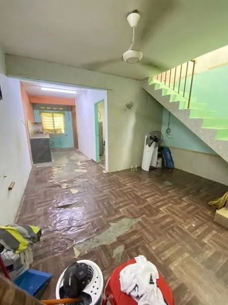 Room features: green painted walls, cream painted walls, wooden parquet flooring, ceiling fan, staircase with green railing, plastic sheet on floor, exposed electrical outlets, window with yellow curtains, open space layout, storage items visible.