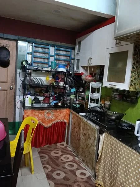 Kitchen features: white cabinets, black countertop, stainless-steel gas stove, built-in oven, dish rack with dishes, kitchen utensils on shelves, green painted walls, decorative curtain, area rug with circular pattern, yellow plastic chair, sink with faucet, microwave, refrigerator, open shelving.