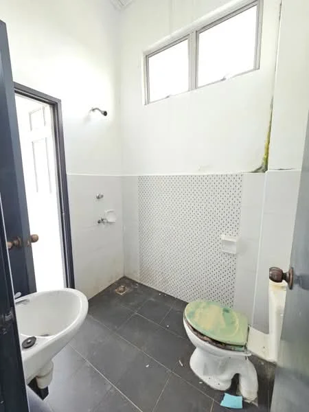 Bathroom features: white painted walls, black tile flooring, single-bowl sink, toilet, exposed plumbing, two wall-mounted faucets, small windows, green toilet seat, mold on walls.