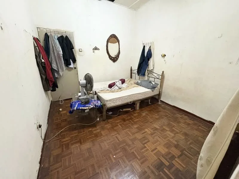Bedroom features: wooden flooring, white painted walls, single bed, metal bed frame, mirror on wall, clothes hanging on hooks, fan, blanket on bed, decorative wall hook.